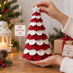 May include: A cone-shaped crochet Christmas tree decoration featuring alternating layers of red and white textured petals, topped with a white crocheted star. The tree measures 13 inches tall, excluding the star, as indicated by a label.