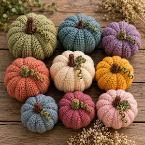 May include: A collection of nine crocheted pumpkins in various colors including sage green, blue, purple, orange, cream, yellow, and pink. Each pumpkin features a brown crocheted stem and a small green curly vine detail on top of the ribbed surface.