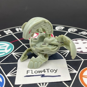 Könnte beinhalten: Ein hellgraues, bewegliches Kunststoff-Kreaturenspielzeug mit einem segmentierten, geschwungenen Kopf und mehreren ausfahrbaren Gliedmaßen. Das Spielzeug hat sichtbare Metallschrauben an den Gelenken und steht hinter einem weißen Etikett mit dem Text Flow4Toy.