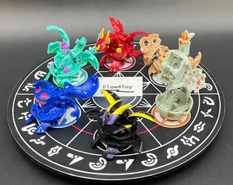 Pode incluir: Uma coleção de seis figuras transformáveis Bakugan em várias cores, incluindo vermelho, azul, verde, preto e bege, dispostas num tabuleiro de jogo circular preto com símbolos brancos e um cartão central branco com o texto Flow4Toy.
