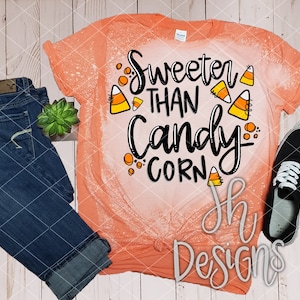 May include: A peach-colored t-shirt with a distressed look featuring the text "Sweeter than Candy Corn" in black with orange and white candy corn graphics.