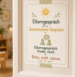 May include: A rectangular white sign taped to a door with green and yellow illustrations of a sun, leaves, hearts, and two figures. The text reads: "Elterngespr&auml;ch f&uuml;r ein Sonnenschein-Gespr&auml;ch", "Elterngespr&auml;ch findet statt.", and "Bitte nicht st&ouml;ren."