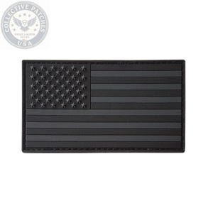 May include: A rectangular morale patch featuring a monochromatic black and dark grey American flag design. The flag consists of raised stars in the canton and horizontal stripes, all rendered in a matte, low-visibility color scheme.