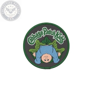 May include: A circular embroidered patch featuring a dark gray background with a green border. The design depicts a baby in a light blue outfit lying on a large green cabbage leaf. The text Cabbage Patch Kids is embroidered in green above.