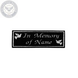 May include: A rectangular black embroidered patch featuring white stitched text that reads In Memory of Name. The design includes a white border and two white dove silhouettes, one positioned on the left side and one on the right side of the text.