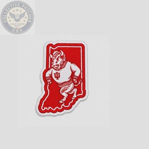 Peut inclure: Un écusson brodé rouge et blanc en forme de l'État de l'Indiana. L'écusson présente un motif de bison portant un pull avec les lettres IU sur la poitrine, sur un fond rouge uni avec une bordure blanche.