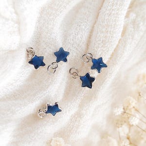 May include: Four small star-shaped charms with a deep blue, translucent finish and silver-toned metal edges. Each charm features a small circular jump ring attached to the top point, allowing for easy connection to jewellery or other decorative items.