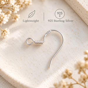 Puede incluir: Un gancho de pendiente de plata con un detalle de alambre enrollado y un pequeño bucle en el extremo. El metal está marcado con el texto 925. El texto en la imagen incluye las palabras Lightweight y 925 Sterling Silver, junto a un icono de pluma.
