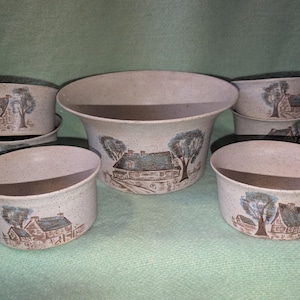 Könnte beinhalten: Ein Set aus fünf beigen, gesprenkelten Keramikschalen mit einer aufgedruckten Illustration eines Hauses mit Schornstein und einem großen Baum. Die Schalen haben einen ausgestellten Rand und eine glatte Oberfläche, wobei die mittlere Schale größer ist.