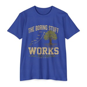 Op de afbeelding: Een koningsblauw t-shirt met korte mouwen en een beige grafische print. Het ontwerp bevat een groeigrafiek met de tekst THE BORING STUFF, een boomillustratie en de tekst WORKS SMALL, STEADY, COMPOUNDS, met labels voor de tijdlijn.