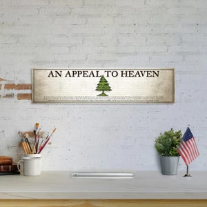 May include: A rectangular wall sign featuring the text AN APPEAL TO HEAVEN in black capital letters, centered above a green pine tree illustration. Below the tree, smaller black text provides historical context on a light beige background.