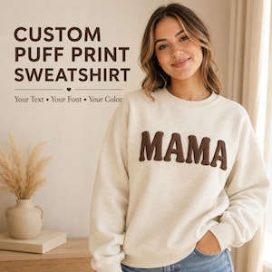 May include: A cream-colored long-sleeve sweatshirt featuring the word MAMA in a dark brown raised puff print on the chest. The text CUSTOM PUFF PRINT SWEATSHIRT, Your Text, Your Font, and Your Color are printed in dark brown on the left side.