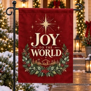 May include: A rectangular deep red garden flag hanging on a black metal stand. The flag features the gold text JOY TO THE WORLD, a large gold star, and a green pine wreath with red berries surrounding a silhouette of a nativity scene.