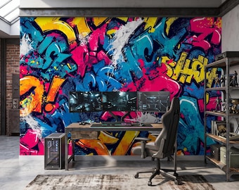 May include: A wall mural featuring vibrant graffiti art in shades of hot pink, bright yellow, and electric blue. The design includes layered abstract shapes, splatters, and stylized lettering. The mural serves as a backdrop for a gaming setup.