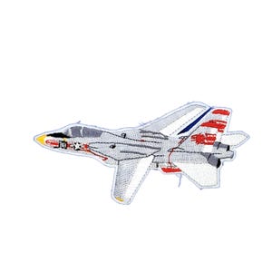 May include: An embroidered patch featuring a gray fighter jet in profile. The aircraft has a yellow nose cone, a dark cockpit canopy, and red and white markings on the tail fin. The design includes a small star emblem near the front section.