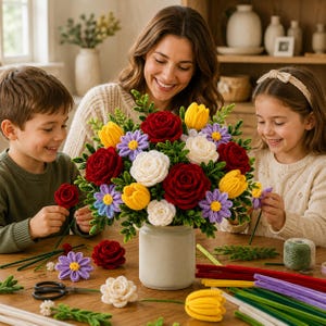 May include: A bouquet of crocheted flowers in a light gray ceramic vase, featuring deep red roses, white roses, yellow tulips, and purple daisies with green stems and leaves. The arrangement is displayed on a wooden table with loose yarn stems.