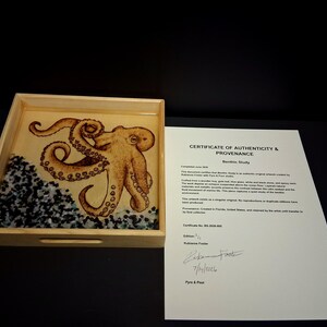 May include: A square wooden tray containing a resin-encased octopus illustration with gold leaf accents and a base of black and white stones. Beside the tray is a white paper Certificate of Authenticity and Provenance titled Benthic Study.
