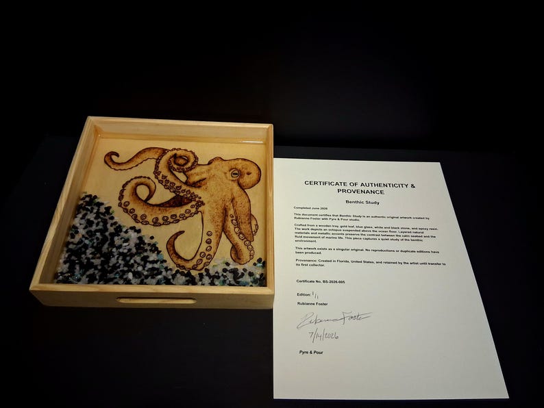 May include: A square wooden tray containing a resin-encased octopus illustration with gold leaf accents and a base of black and white stones. Beside the tray is a white paper Certificate of Authenticity and Provenance titled Benthic Study.