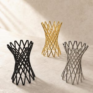 Pode incluir: Três suportes cilíndricos construídos com fio de metal fino num padrão de treliça cruzada. Um suporte é preto mate, um é dourado polido e um é prateado polido. Cada um apresenta uma abertura superior larga com borda em ziguezague.