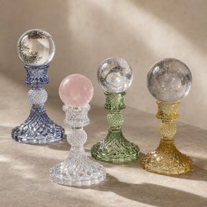 Peut inclure: Quatre supports décoratifs en verre avec des bases texturées à motif diamant en bleu, transparent, vert et ambre. Chaque support soutient une sphère lisse en pierre ou en verre, incluant une sphère transparente, un quartz rose et deux sphères en cristal.