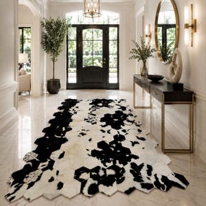 May include: A large area rug composed of numerous hexagonal tiles featuring a black and white cowhide pattern. The rug is laid out on a polished light-colored floor, showcasing a repeating geometric arrangement of individual hide patches.