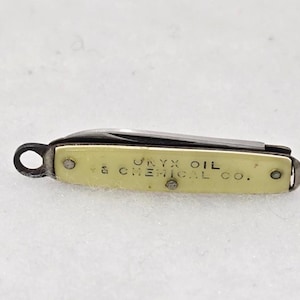 May include: A small, vintage pocket knife with a cream-colored handle and a partially open blade. The handle is inscribed with "Onyx Oil & Chemical Co." in black lettering. The knife has a small loop for attaching to a keychain.