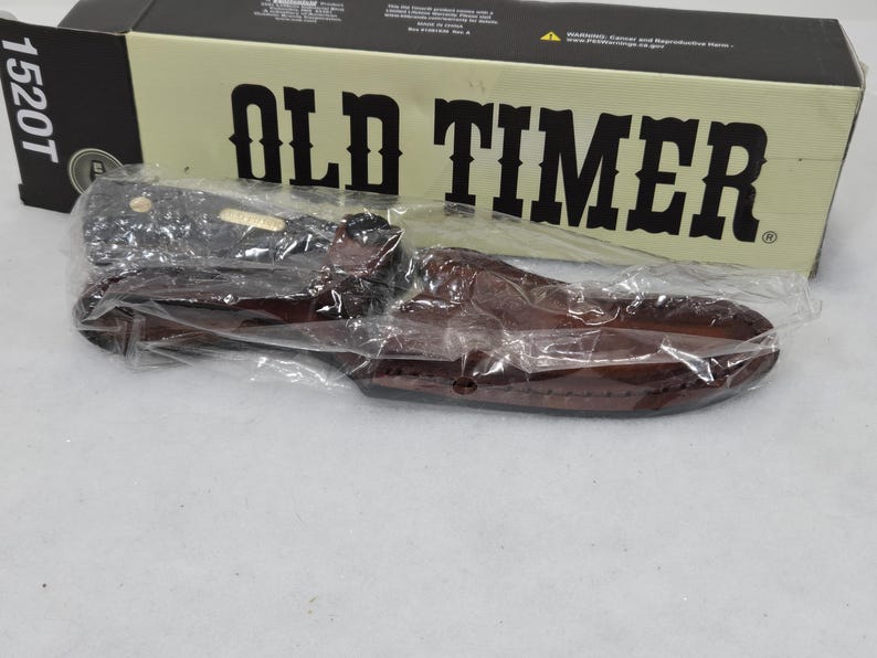 May include: A new Old Timer knife in a brown leather sheath, packaged in a black and tan box. The box has the words "OLD TIMER" in large, bold letters.