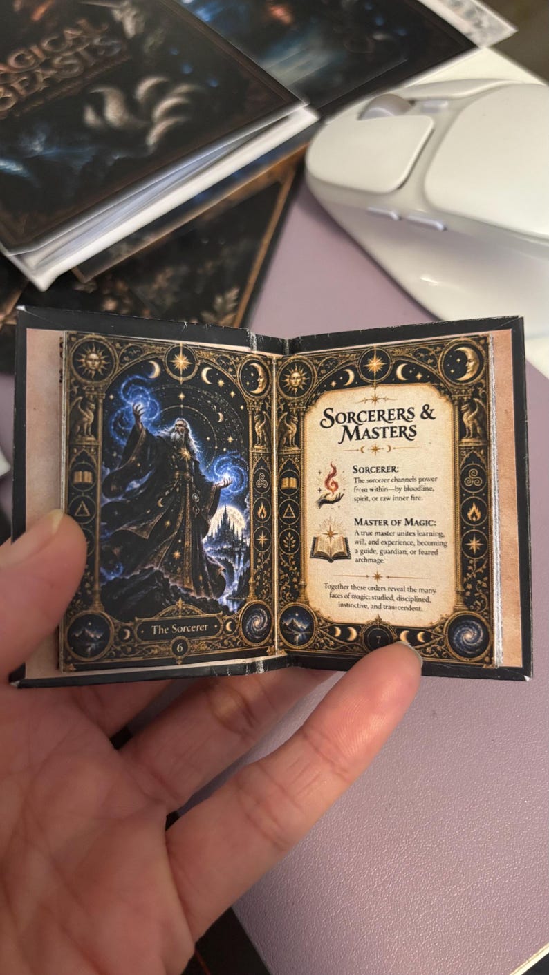 May include: A miniature open book featuring an illustration of a sorcerer casting blue magic on the left page and the text Sorcerers & Masters with descriptions of a sorcerer and master of magic on the right page, framed by gold celestial motifs.
