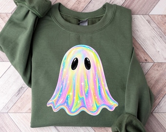 May include: An olive green crewneck sweatshirt featuring a central graphic of a ghost with a holographic, iridescent finish. The ghost has two large, solid black oval eyes and a shimmering, multi-colored surface with small white star accents.