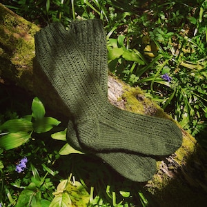 May include: A pair of olive green knitted socks featuring a vertical ribbed pattern throughout the leg and foot. The socks are constructed with a reinforced heel and toe section, showcasing a consistent knit texture and a deep, earthy color tone.