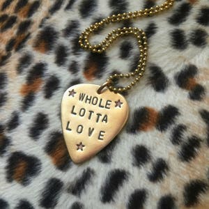 May include: A gold necklace with a guitar pick pendant that says "WHOLE LOTTA LOVE" with stars on either side.