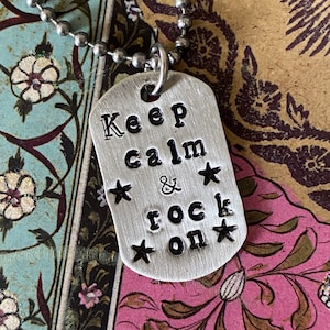 May include: A silver necklace with a silver tag pendant that reads "Keep calm & rock on" with stars around the text.