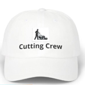 May include: A white baseball cap featuring a black graphic of a person operating a lawnmower centred above the text "Cutting Crew" in a bold, black sans-serif font. The cap has a curved brim and a structured crown with a button on the top.