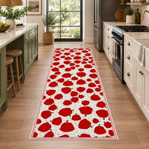 Peut inclure: Un long tapis de couloir rectangulaire présentant un motif répétitif de citrouilles rouge vif sur un fond crème. Le tapis est encadré par une fine bordure rouge et est posé sur un sol en bois dans une cuisine avec des placards.