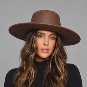 May include: A solid brown wide-brimmed hat with a structured crown and a flat brim. The hat features a smooth, matte finish and a clean, minimalist design with tonal stitching along the top of the crown and the edge of the brim.