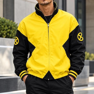 Peut inclure: Une veste zippée jaune et noire avec un col montant, des manches longues à poignets noirs ornés de deux bandes jaunes, et un emblème circulaire jaune et noir du logo X-Men sur chaque épaule. La veste présente un design bicolore.