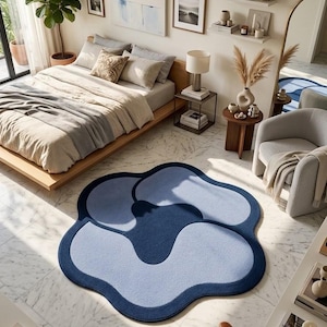 May include: A large, flower-shaped area rug featuring a layered design in shades of dark navy blue and light periwinkle blue. The rug has a soft, textured surface with smooth, rounded edges, creating a distinct organic shape on the floor.