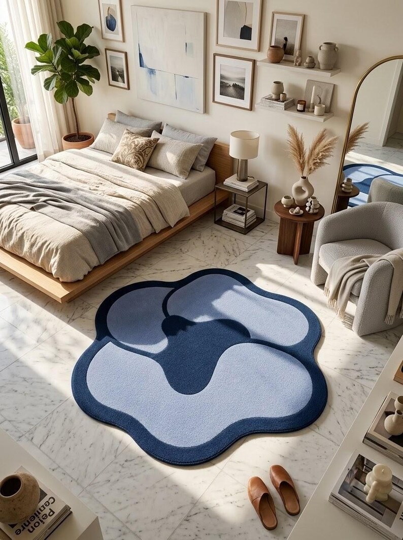 May include: A large, flower-shaped area rug featuring a layered design in shades of dark navy blue and light periwinkle blue. The rug has a soft, textured surface with smooth, rounded edges, creating a distinct organic shape on the floor.