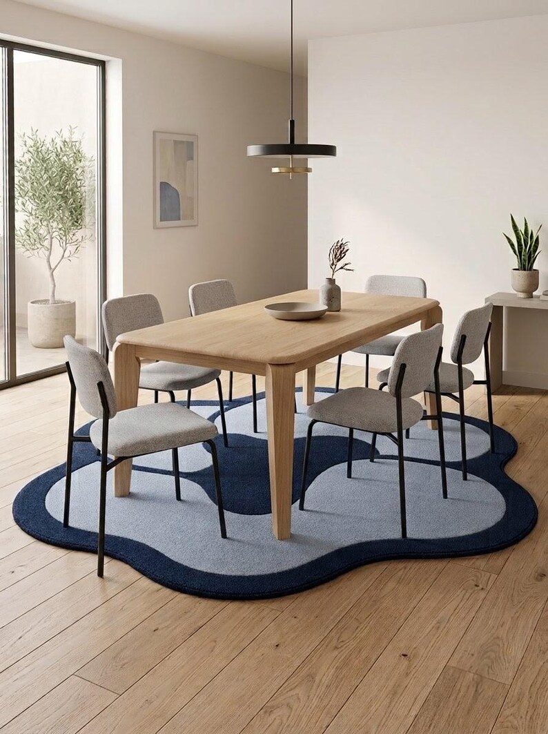 May include: A rectangular light wood dining table with four tapered legs, surrounded by six chairs featuring light gray upholstered seats and black metal frames, placed on a large, irregular, cloud-shaped rug in shades of navy and light blue.