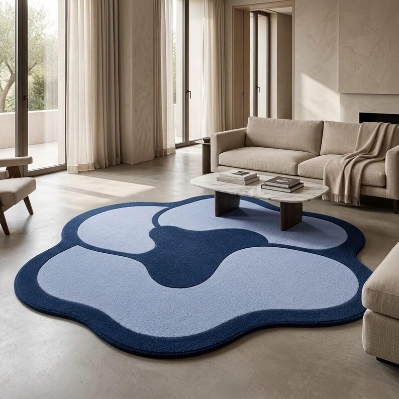 May include: A large, floor-based area rug with an organic, cloud-like shape. The rug features a deep navy blue border and central accent, contrasting with lighter periwinkle blue sections that fill the remaining curved, petal-like segments.