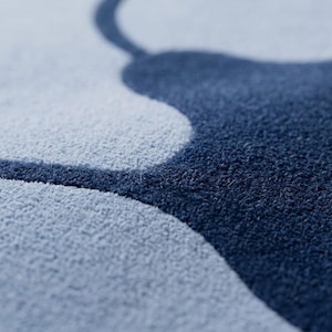 May include: A close-up view of a textured rug featuring a high-contrast design with large, organic shapes in deep navy blue and light gray. The surface has a dense, tufted pile construction that creates a soft, tactile appearance throughout.