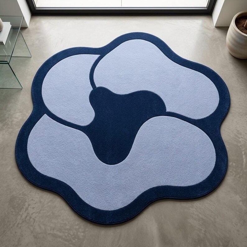 May include: A circular area rug with an irregular, wavy edge featuring a dark navy blue border and a central dark navy blue shape surrounded by four light blue, rounded, petal-like sections that create a cohesive, abstract floral pattern.
