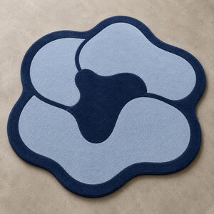 May include: A flower-shaped area rug featuring a dark navy blue border and central core with three light blue petal-like sections. The rug has a soft, tufted texture and a distinct organic, curved outline that defines its overall floral silhouette.