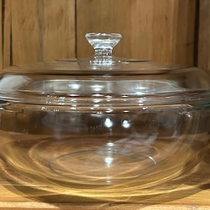 May include: A clear glass casserole dish with a matching lid and side handles. A metal ruler is positioned vertically next to the dish, showing the height of the lid is approximately 3 inches and the total height is about 4 inches.