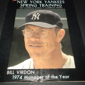 May include: A black and white photo of Bill Virdon, the 1974 Manager of the Year for the New York Yankees. He is wearing a New York Yankees baseball cap and a white and black striped shirt. The photo is from the 1975 New York Yankees Spring Training program.