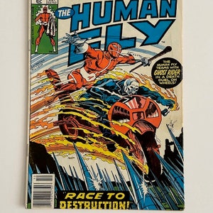 May include: A comic book cover featuring a red and white superhero, The Human Fly, riding a motorcycle with a flaming trail. The cover text reads "The Human Fly" and "Race to Destruction!" The comic book is from Marvel Comics Group and is issue number 2, October 1977.