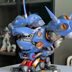 Può includere: Un action figure robotica blu e grigia con una punta prominente sulla testa, grandi propulsori sulle spalle con prese d'aria color rame e la scritta OB 02 stampata sul petto. Il design meccanico include cavi rossi esposti e articolazioni.