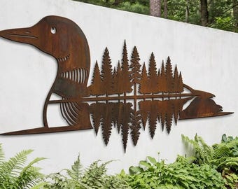 Puede incluir: Una pieza de arte mural de metal color óxido con forma de silueta de colimbo. El cuerpo del ave presenta un diseño recortado detallado de un bosque de pinos, con un efecto de reflejo invertido debajo de la línea de los árboles, creando un patrón simétrico.