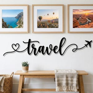 May include: A black metal wall sign featuring the word travel in cursive script, with a heart shape at the beginning and an airplane silhouette at the end. Above the sign are three framed landscape photographs showing a coastal view, hot air balloons, and a canyon.