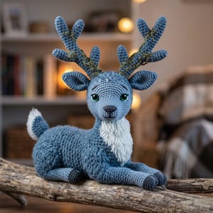 May include: A blue crocheted deer plush toy with large antlers featuring green accents. The deer has a white chest patch, a small white-tipped tail, and dark green eyes. It is crafted with a textured yarn finish and sits in a resting position.
